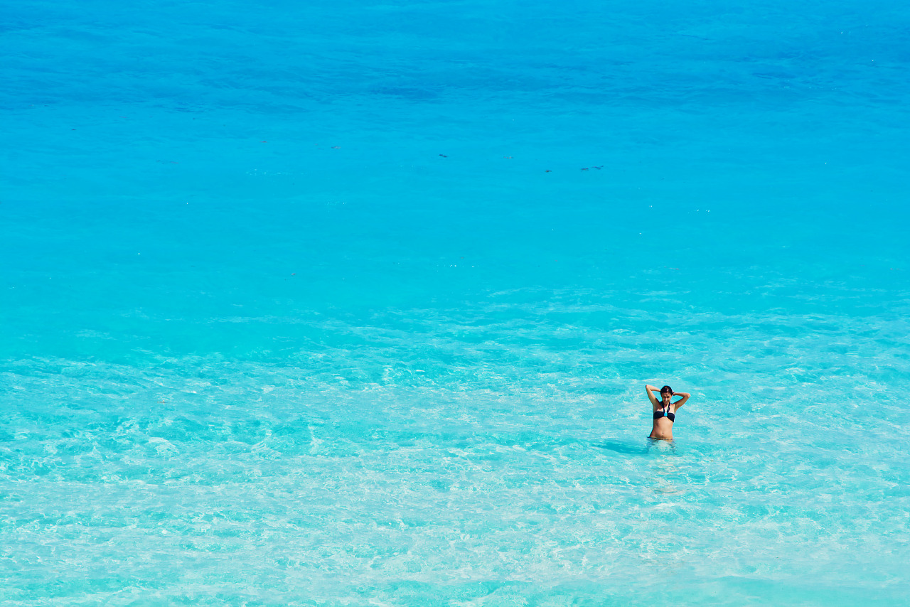 Girl alone in clear turquoise water at the beach of Cancún Mexico